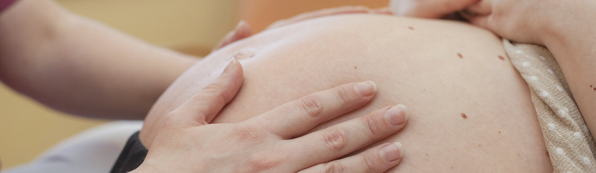Hebamme tastet Bauch der werdenden Mutter ab.