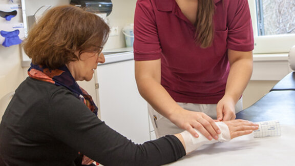 Eine Medizinische Fachangestellte legt einen Verband an der Hand einer Patientin an.