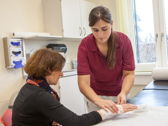 Eine Medizinische Fachangestellte legt einen Verband an der Hand einer Patientin an.
