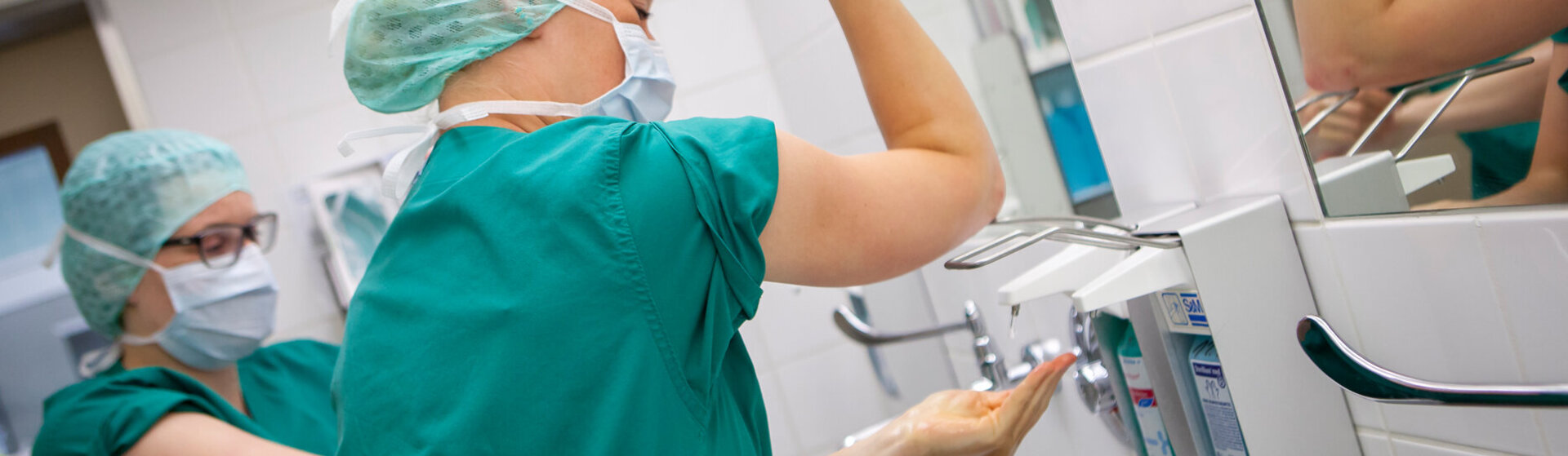 Zwei medizinische Fachkräfte bereiten sich auf eine OP vor und desinfizieren sich Hände und Arme. Zwei medizinische Fachkräfte bereiten sich auf eine OP vor und desinfizieren sich Hände und Arme.