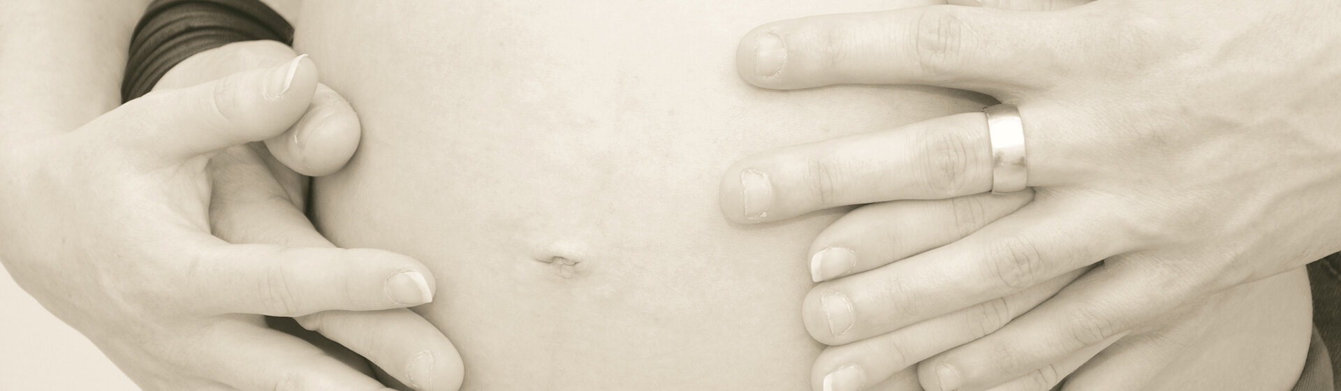 Hände von Mutter und Vater umfassen den Babybauch.