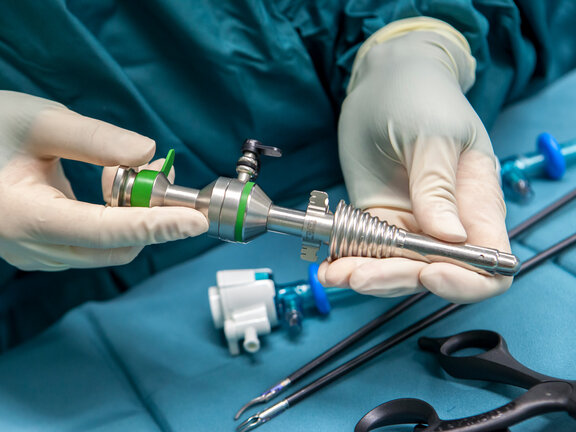Hände in Latexhandschuhen am OP-Tisch halten ein Trokar (Hülse) für ein Laparoskop für das minimalinvasive Vorgehen bei einer Leistenhernie.
