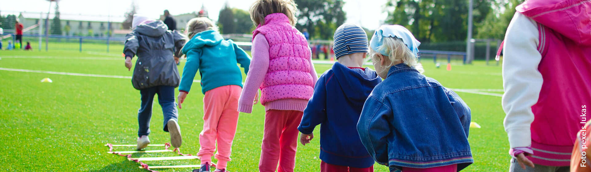 Kinder auf einer grünen Wiese in einer Reihe hintereinander machen ein Geschicklichkeits- und Hüpfspiel. Kinder auf einer grünen Wiese in einer Reihe hintereinander machen ein Geschicklichkeits- und Hüpfspiel.