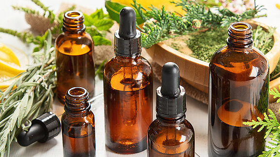 Mehrere kleine Flaschen mit Ölen, umgeben von Kräutern und Naturmaterialien
