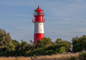 Rot-weißer Leuchturm hinter grünen Büschen vor blauem Himmel