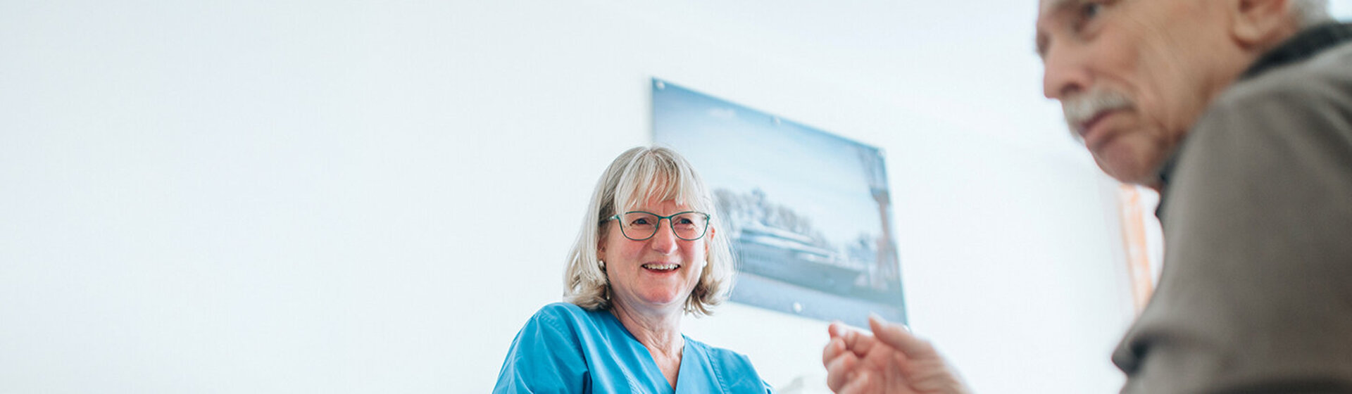 Patient sitzt im Rollstuhl, Pflegefachkraft lächelt ihn an und und gibt ihm einen Gehwagen. Patient sitzt im Rollstuhl, Pflegefachkraft lächelt ihn an und und gibt ihm einen Gehwagen.