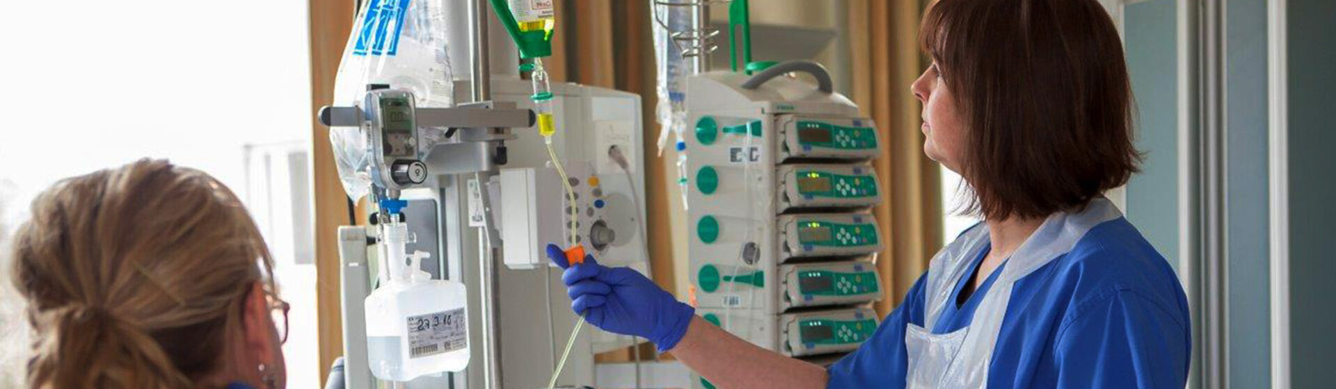 Eine Mitarbeiterin kontrolliert die Überwachungsgeräte, eine Mitarbeiterin kümmert sich um der/dem PatientIn.