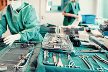 OP-Instrumente liegen auf grünem Tuch, im Hintergrund zwei MitarbeiterInnen. OP-Instrumente liegen auf grünem Tuch, im Hintergrund zwei MitarbeiterInnen.