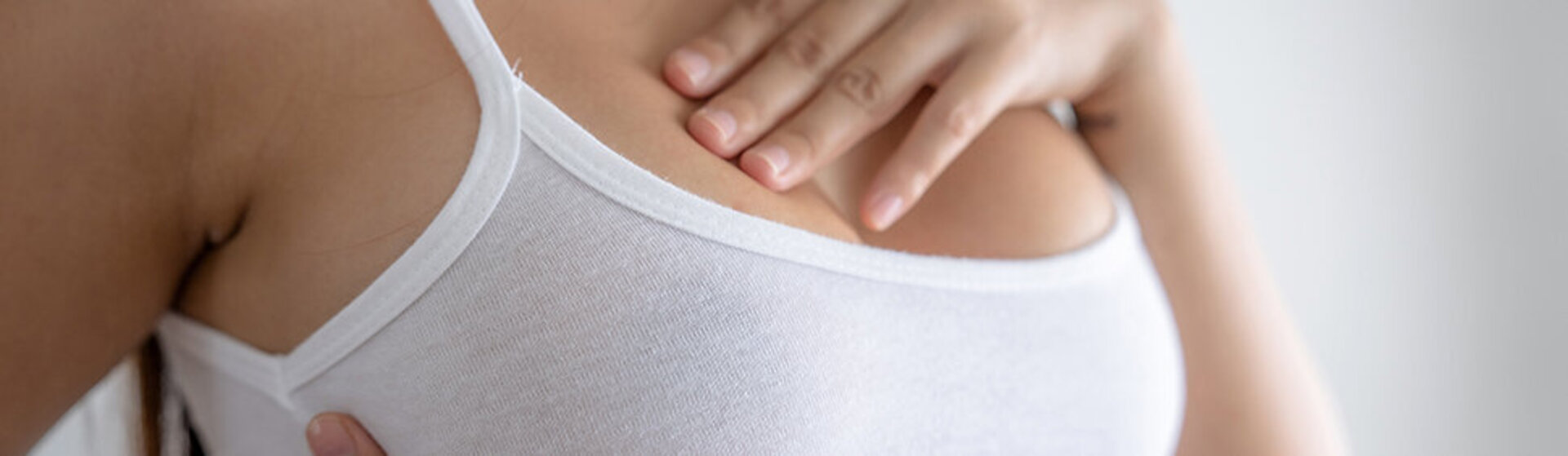 Frau im Unterhemd fühlt ihre Brust ab.