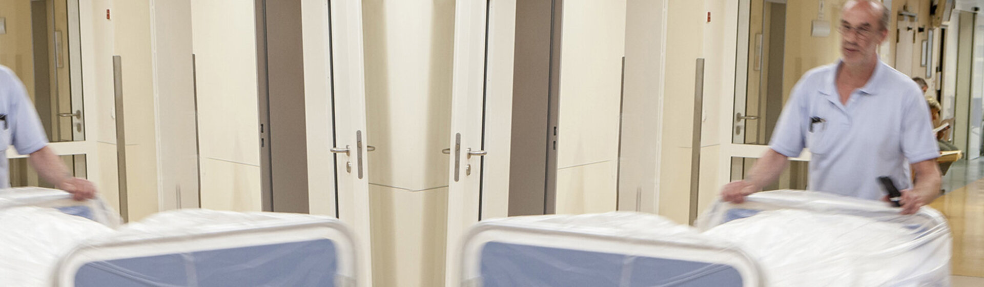 Ein Mitarbeiter des Transportdienstes schiebt ein leeres Bett.