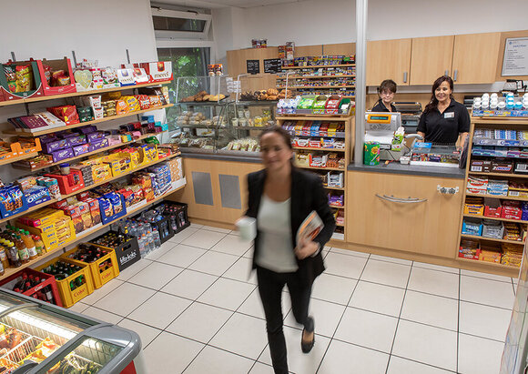 Kiosk Eine Besucherin hat im Kiosk eingekauft, hinterm Tresen stehen zwei Mitarbeitende.