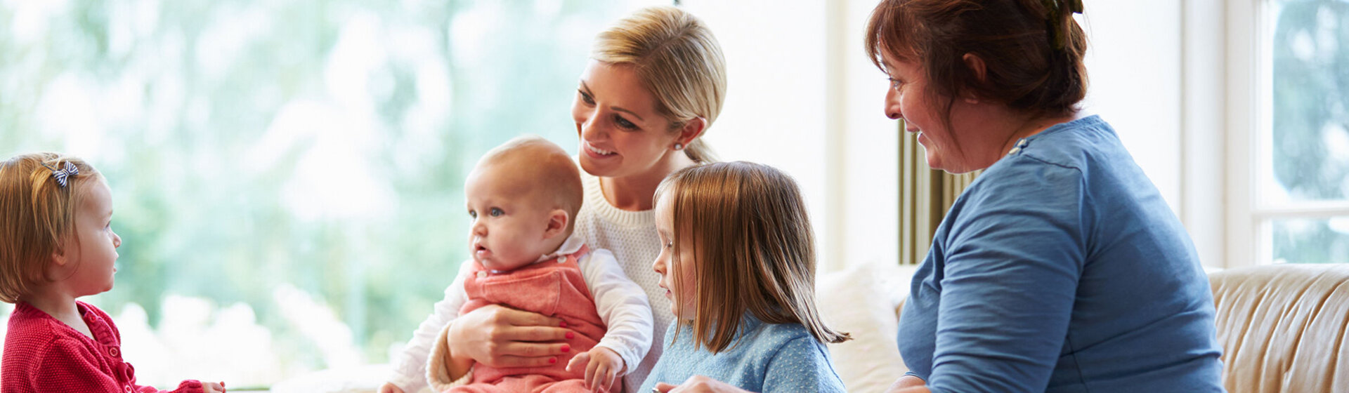 Zwei Frauen sitzen mit drei Kindern unterschiedlichen Alters in einem hellen Wohnzimmer