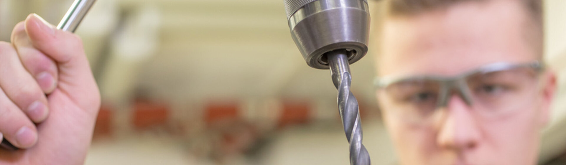 Ein Mitarbeiter mit Schutzbrille bohrt in ein kleines Blech. Ein Mitarbeiter mit Schutzbrille bohrt in ein kleines Blech.