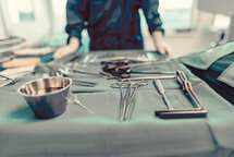 OP-Instrumente liegen auf einem grünen Tuch, im Hintergrund steht ein MitarbeiterIn. OP-Instrumente liegen auf einem grünen Tuch, im Hintergrund steht ein MitarbeiterIn.