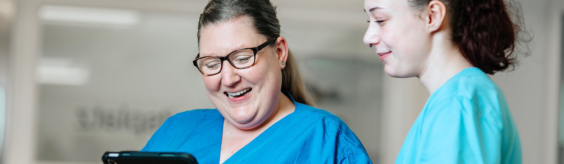 Zwei Pflegefachkräfte schauen lächelnd auf ein Tablett.