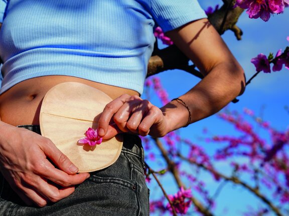 Person hält eine runde Scheibe mit einer Blüte vor dem Bauch als Symbol für das Leben mit einem Stoma