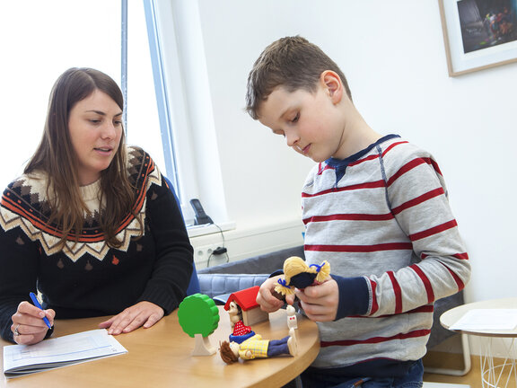 Eine Psychologin unterhält sich mit einem Jungen, der mit Spielzeugfiguren spielt.