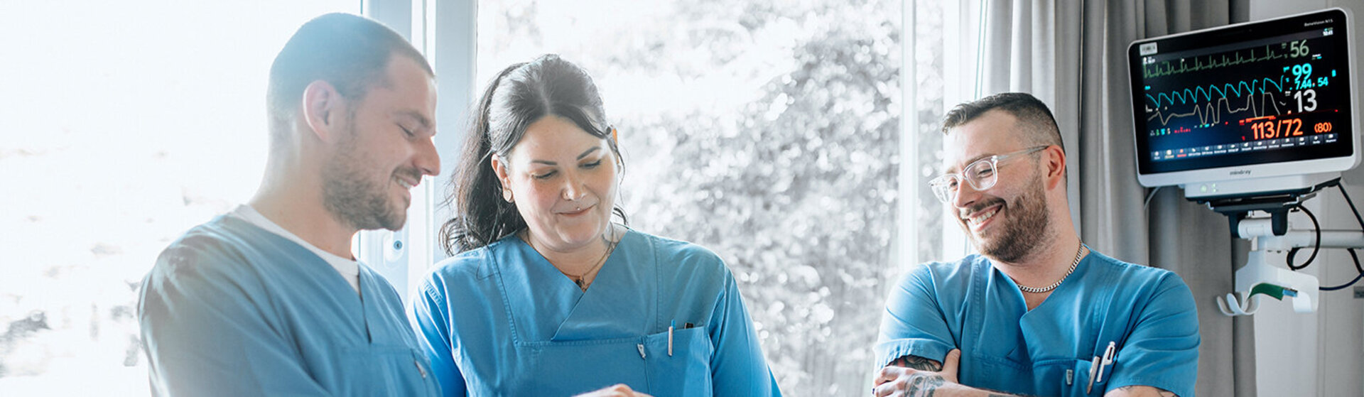 Drei Pflegefachkräfte schauen auf einen Monitor. Drei Pflegefachkräfte schauen auf einen Monitor.