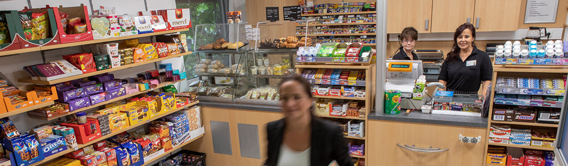 Eine Besucherin hat im Kiosk eingekauft, hinterm Tresen stehen zwei Mitarbeitende. Eine Besucherin hat im Kiosk eingekauft, hinterm Tresen stehen zwei Mitarbeitende.