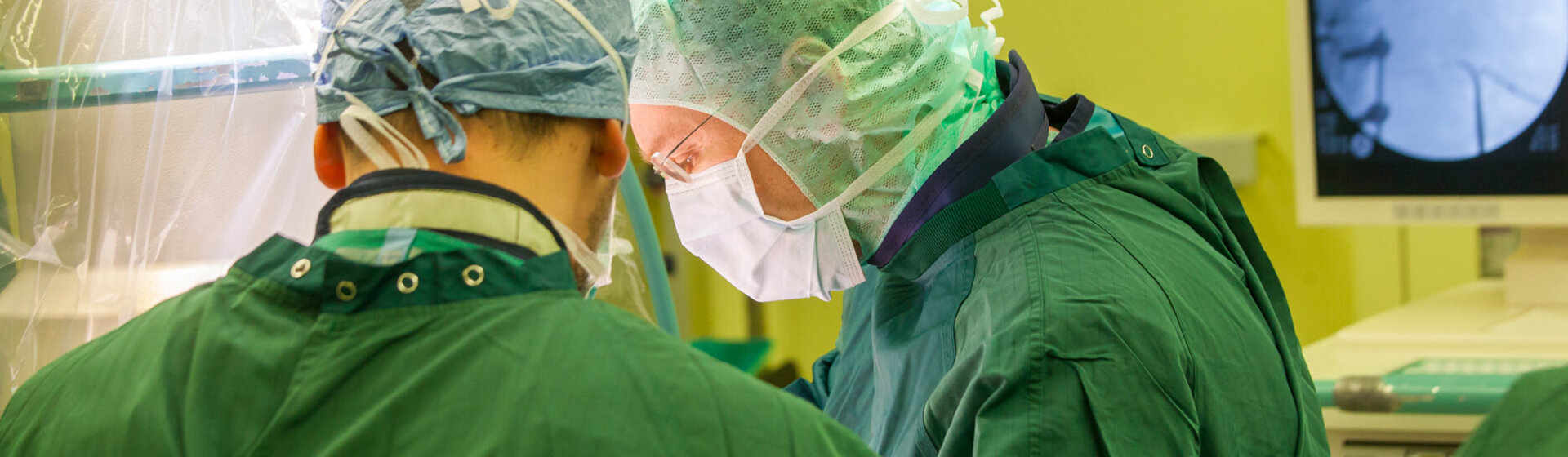 Zwei Operateure in OP-Kleidung im OP-Saal sind konzentriert auf die Operation. Zwei Operateure in OP-Kleidung im OP-Saal sind konzentriert auf die Operation.