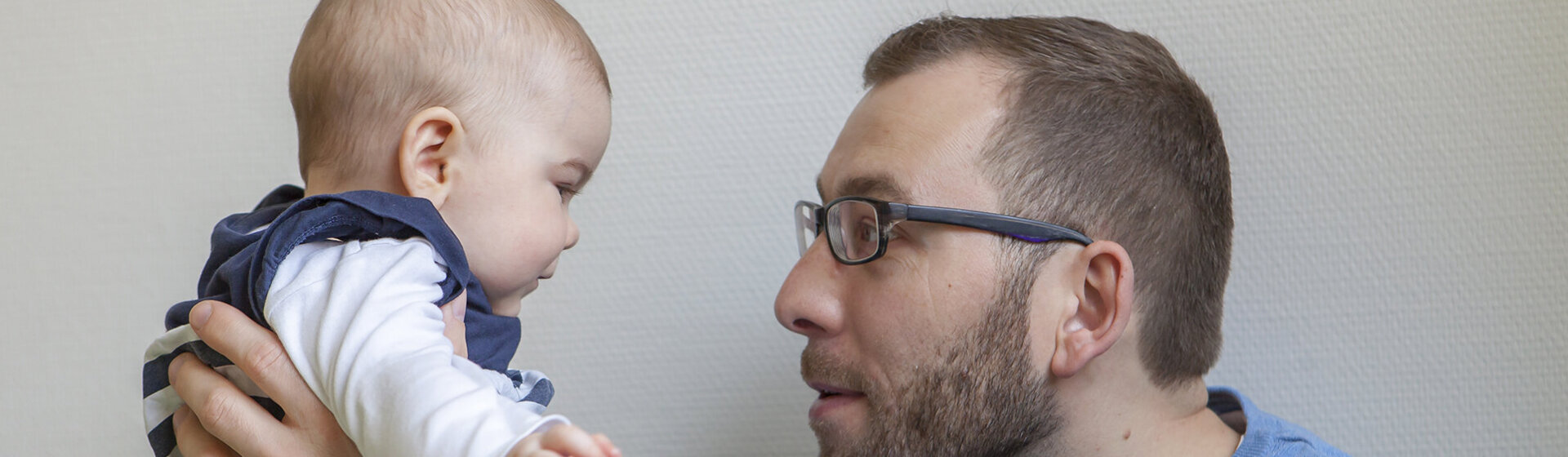 Ein junger Vater hält sein Baby hoch und blickt ihm in die Augen.