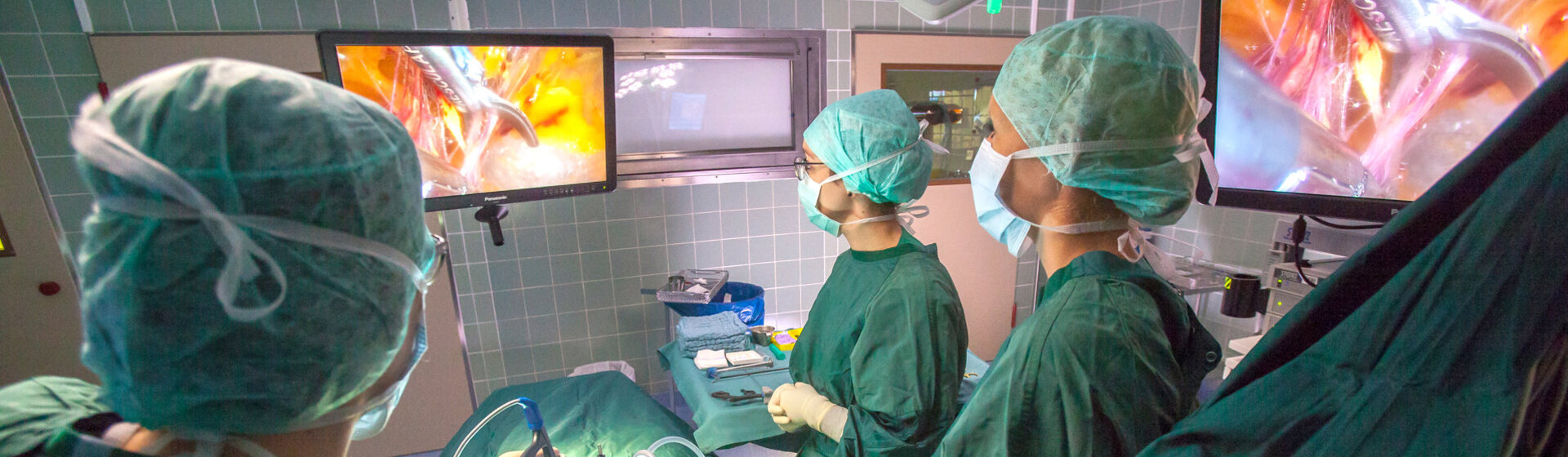 Operationssituation eines Minimal-invasiven Eingriffs, Operateur und medizinische Fachkräfte blicken auf den OP-Monitor.