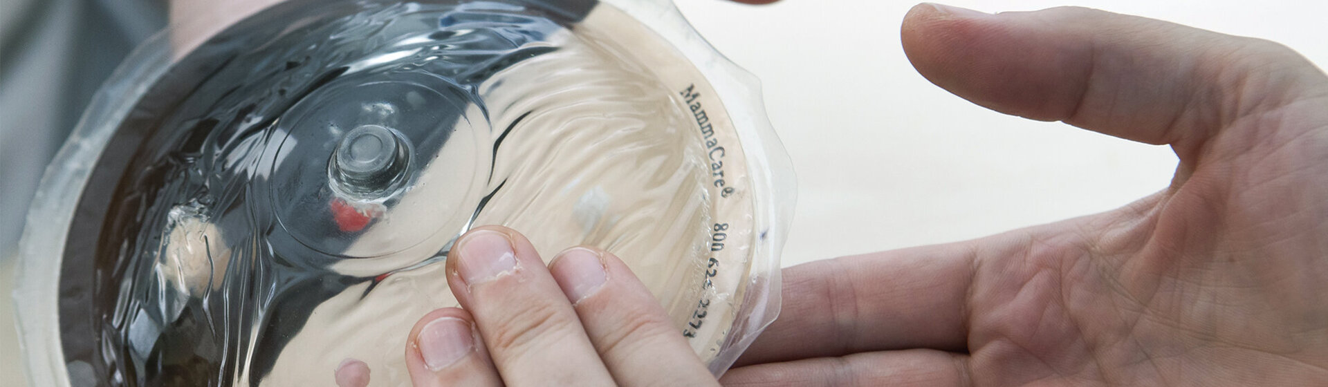 Hände tasten ein Brustmodell ab.