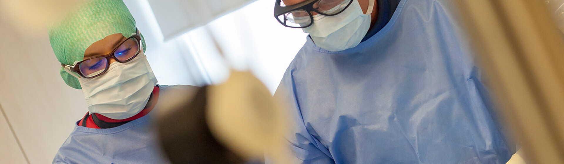 Zwei ÄrztInnen im OP-Kittel mit OP-Haube und OP-Maske bei einer Operation Zwei ÄrztInnen im OP-Kittel mit OP-Haube und OP-Maske bei einer Operation