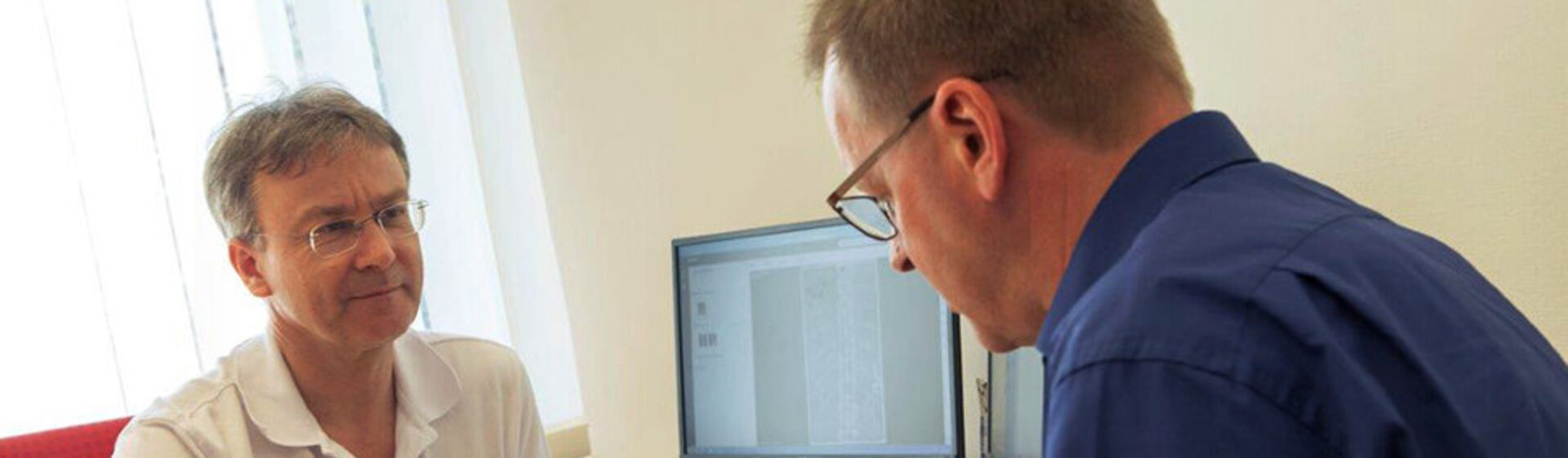 Arzt sitzt mit einem Patienten am Tisch und erklärt die Behandlungsmethode.