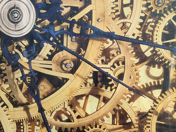 Zahnräder einer Uhr greifen ineinander, darüber sind blaue Zeiger abgebildet.