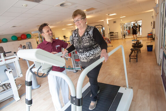 Ein Physiotherapeut leitet eine Patientin auf dem Laufband im MediFit an.