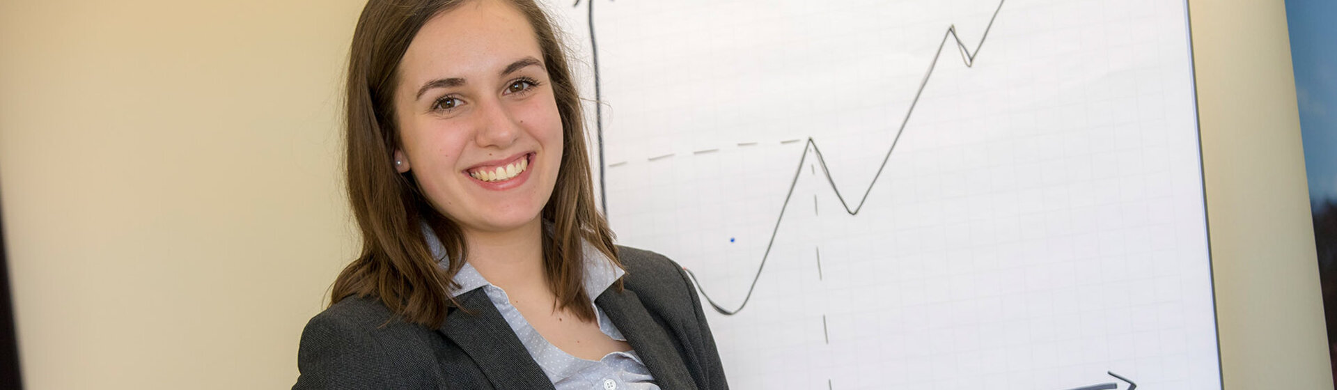 Eine Mitarbeiterin hält lächelnd einen Stift in der Hand - im Hintergrund steht ein Flipchart. Eine Mitarbeiterin hält lächelnd einen Stift in der Hand - im Hintergrund steht ein Flipchart.