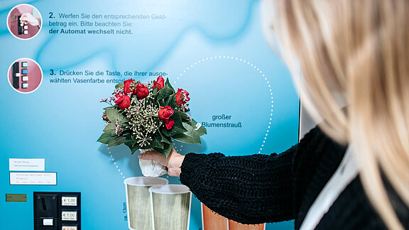 Eine Besucherin bedient den Automaten, an dem man Einmalblumenvasen kaufen kann