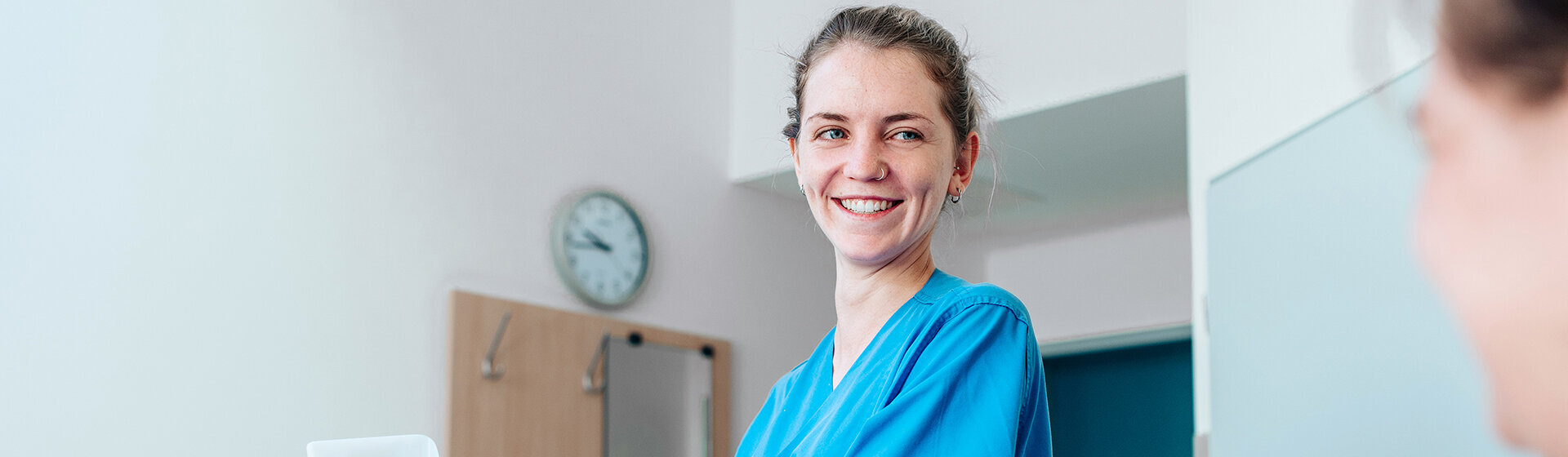 Pflegefachkraft lächelt PatientIn mit hochgelagertem Bein an.