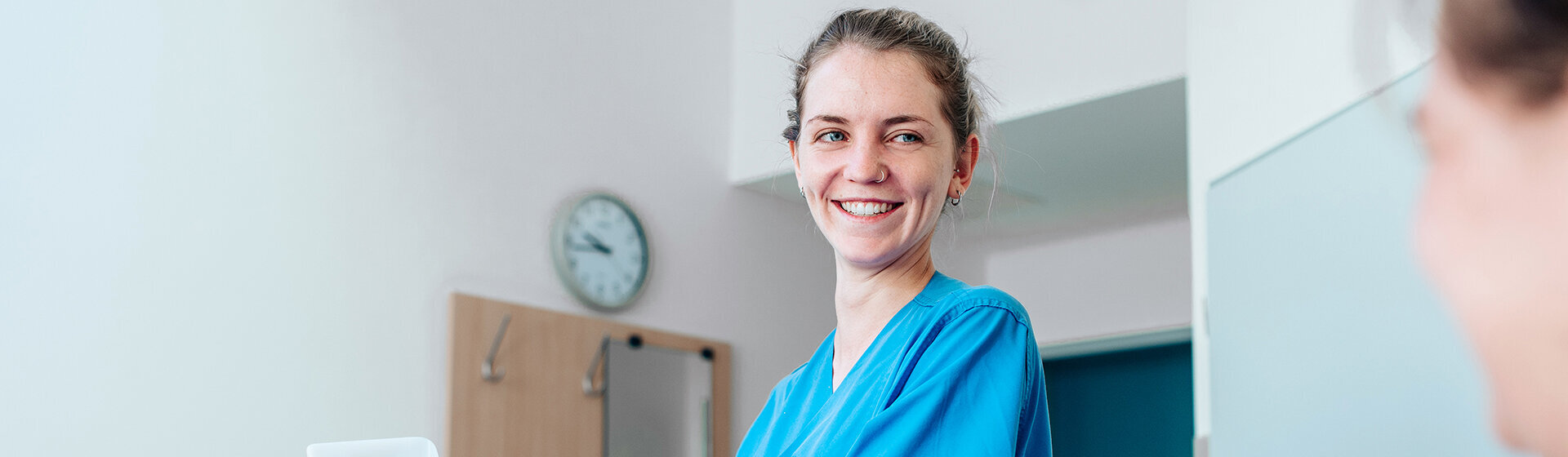 Pflegefachkraft lächelt PatientIn mit hochgelagertem Bein an.