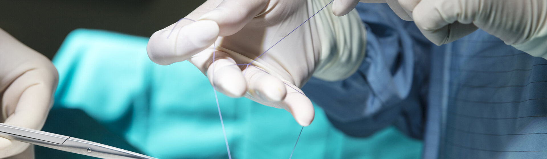 Hände mit OP-Handschuhen nähen eine Wunde.