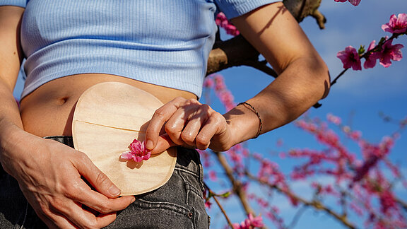 Eine Person legt ihre Hand schützend auf den Bereich um das Stoma und hat eine Blüte in der Hand.