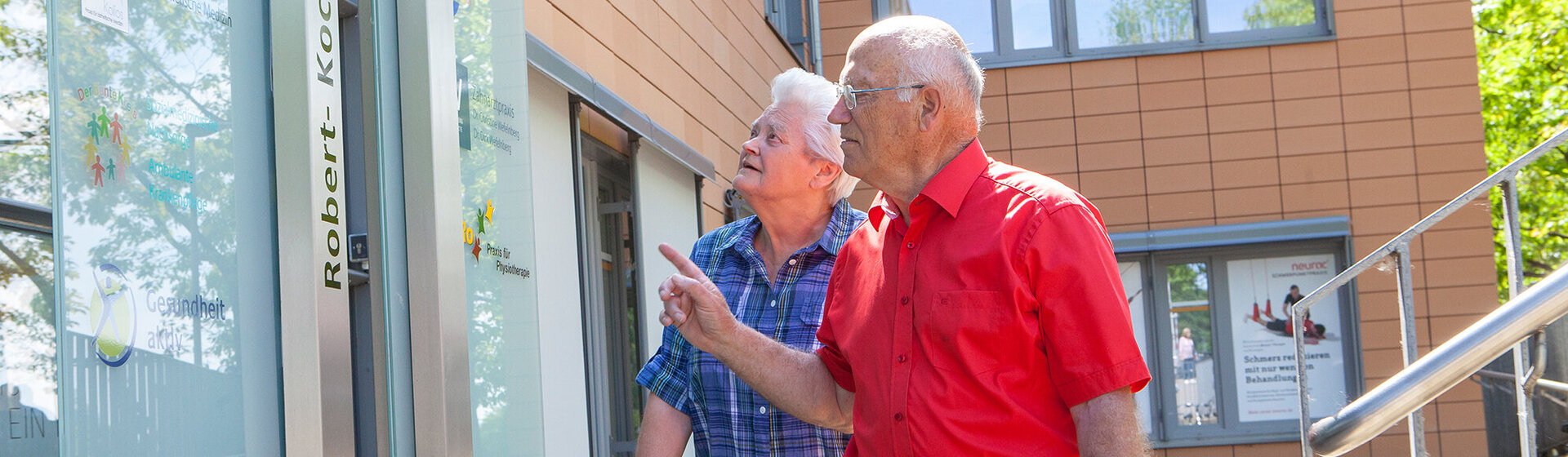 Ein Mann und eine Frau mit Rollator stehen vor dem Ärzte- und Dienstleistungszentrum.