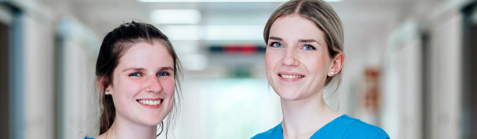 Zwei Pflegefachkräfte lächeln ins Bild.